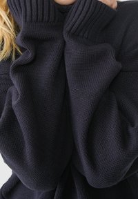 Przeoversizowy ciemnogranatowy sweter z wysokim, prążkowanym kołnierzem i fakturowanym wzorem dzianiny. Luźne rękawy tworzą przytulny, zwiewny wygląd.