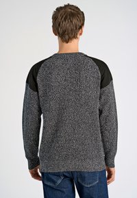 Neulepaita mustana ja harmaana, jossa on teksturoitu kappale ja sileät mustat olkapääkoristeet. Pitkät hihat ja pyöreä kaula-aukko.