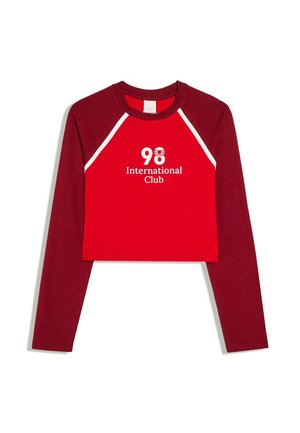 Red and dark red long-sleeve cropped shirt with white text "98 International Club" on the front and white stripes on the shoulders.