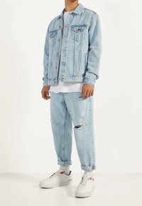 Ljusblå denimjacka med två bröstfickor, matchande slitna ljusblå jeans. Vita sneakers med röda accenter.