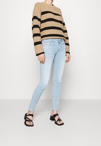 Gebreide beige trui met zwarte horizontale strepen, gecombineerd met lichtblauwe skinny jeans en zwarte sandalen met hak en banddetails.