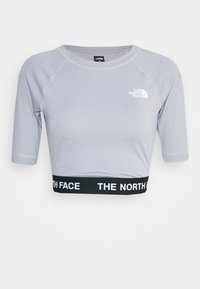 Camiseta deportiva acortada de color púrpura claro con mangas cortas, con un dobladillo elástico negro que presenta el logo en blanco de "The North Face" y el logo de la marca en el pecho.