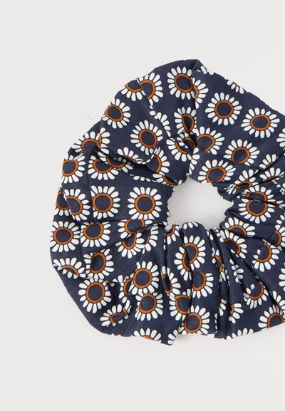 Chouchou en tissu bleu marine avec un motif de fleurs de marguerite blanches et orange sur un fond blanc.