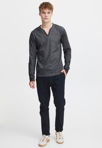 Langarm, dunkelgraues Henley-Shirt mit einer Dreiknopf-Leiste. Getragen mit dunklen Hosen und hellen Sneakers. Einfacher, lässiger Schnitt.