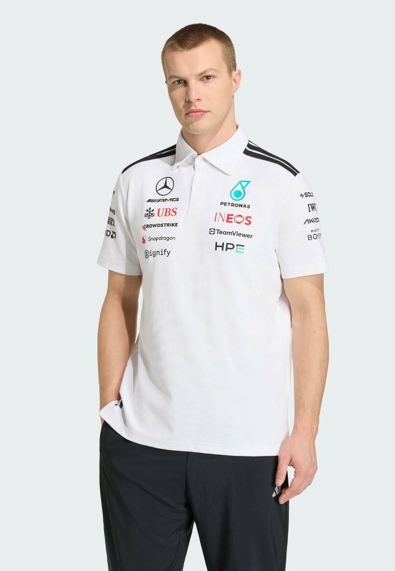 Polo blanc avec col, présentant des accents noirs sur les épaules et divers logos de sponsors imprimés sur le devant. Pas de motifs, texture lisse.