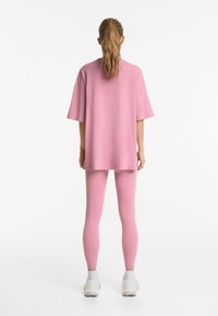 Tricou oversized roz cu mâneci scurte, asortat cu colanți roz. Ținuta se remarcă printr-o textură moale și o siluetă fluidă.
