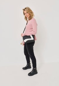 Bocanci negri până la gleznă cu o talpă groasă, asortați cu blugi negri strâmți și un pulover roz deschis. Geanta de umăr are un accent diagonal alb.