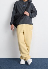 Grå huvtröja med blå logotyp, tillsammans med gula mjukisbyxor och vita sneakers. Svart axelremsväska hängd över axeln.