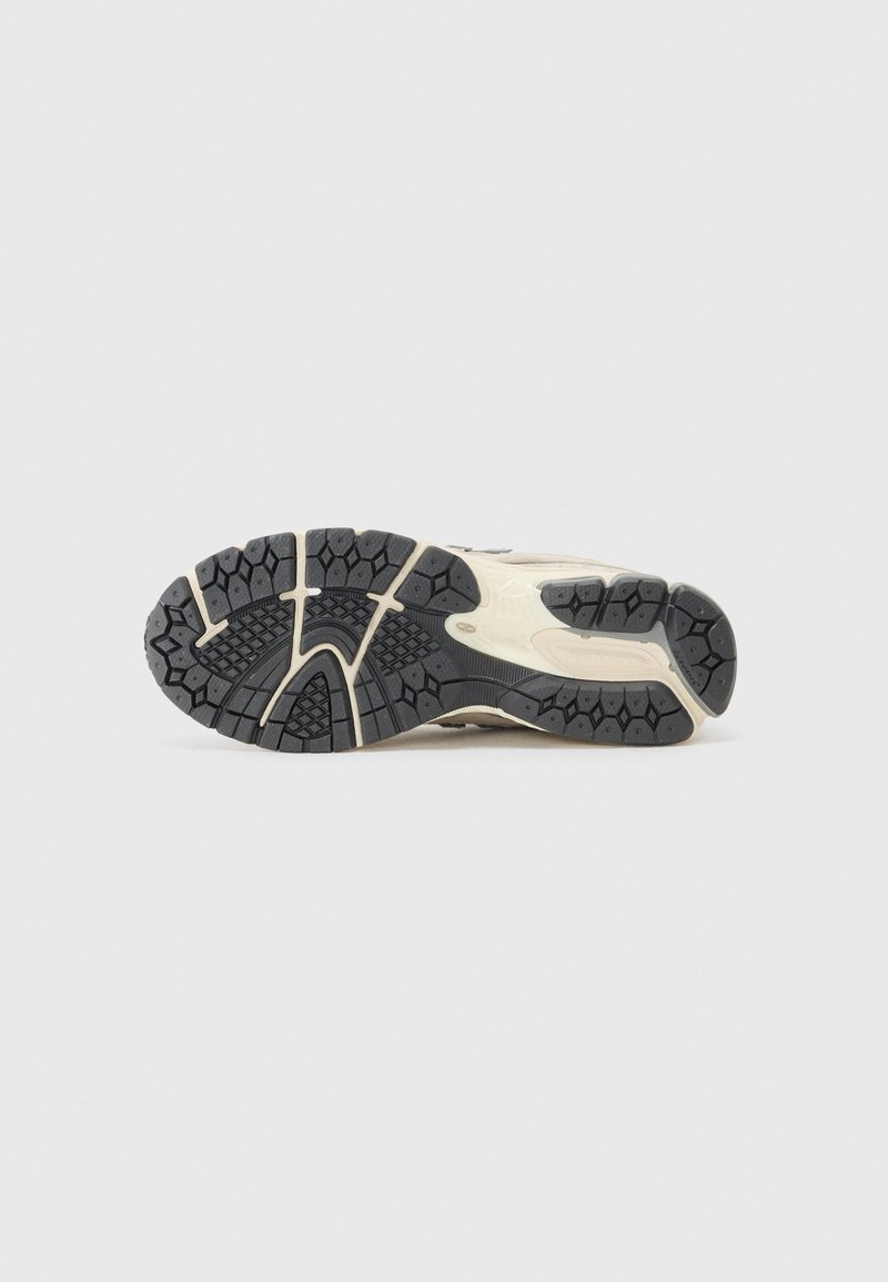 Semelle en caoutchouc noir avec un motif de grip texturé, présentant une semelle intermédiaire crème et des accents blancs, montrant un design de tread détaillé et des courbures.