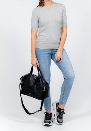 Sac à main en cuir noir avec deux poignées, une bandoulière amovible et une surface texturée. Chemise grise à manches courtes et jean skinny bleu clair portés.