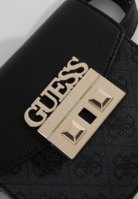 Sort tekstureret håndtaske med guldfarvet GUESS-logo og nitteret lukning.