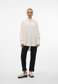 Ivory oversized sweater with a high neck, ribbed cuffs, and hem; paired with black tapered pants and light-colored loafers.