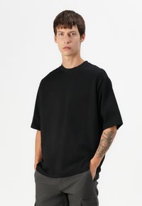 T-shirt noir à manches courtes avec un col rond, en coton. Présente une coupe décontractée et un design minimaliste, sans graphiques ni embellissements.