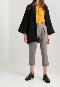 Černý oversized kimono kabát, žlutá blůza s vázacími límci, šedé kostkované cropped kalhoty a černé platformové boty.