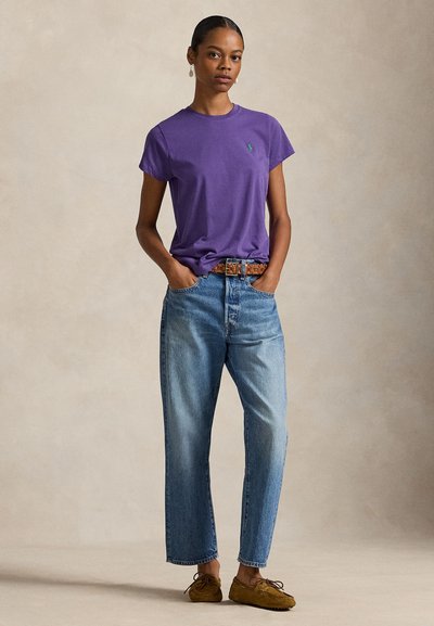 Μωβ βαμβακερό μπλουζάκι με στρογγυλή λαιμόκοψη, συνδυασμένο με ψηλόμεσο ανοιχτό μπλε τζιν παντελόνι, με καφέ ζώνη με σχέδιο και καφέ παπούτσια.