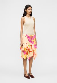 Haut beige sans manches, jupe à volants fleurie rose et pêche avec ourlet asymétrique, et chaussures à brides marron. Design simple avec des motifs vibrants.