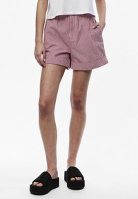 Pantaloni corti a righe rosse e bianche con una vestibilità comoda, dotati di cintura elastica e tasche laterali. Abbinati a sandali platform neri.