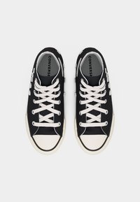 Μαύρα χαμηλά sneakers Converse με λευκά κορδόνια και σόλες, διακοσμημένα με μικρές λευκές λεπτομέρειες στις πλευρές από καμβά.