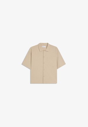 Beige kortærmet skjorte med knapper, krave og enkelt brystlomme, vist fladt på hvid baggrund.