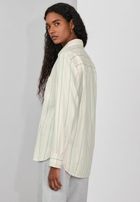 Svītrains krekls ar pogām mīkstā pasteļtoņu krāsā. Izgatavots no viegla auduma ar brīvu siluetu un vienu krūšu kabatu; izliektām malām.