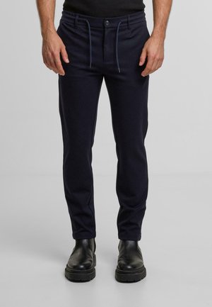 Pantaloni blu in tessuto elasticizzato e testurizzato, dotati di coulisse e chiusura con bottone, gamba affusolata e tasche laterali. Stivali neri.