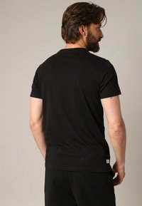 Zwarte t-shirt met korte mouwen, gemaakt van zachte katoen, met een klassieke ronde hals en een klein merklabel aan de onderzoom. Eenvoudig ontwerp.