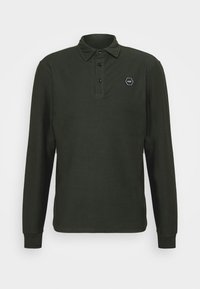 Camisa polo de manga larga en verde oscuro, con un cuello abotonado, tres botones y un parche de logo hexagonal en el pecho.