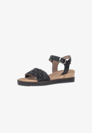 Black leather sandal with woven front strap, adjustable ankle buckle, cork wedge heel, and ridged black sole on white background.