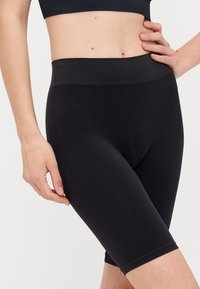 Black mid-thigh leggings made of smooth, stretchy fabric with a wide waistband. Minimalist design, no visible patterns or hardware details.