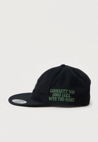 Black Carhartt WIP snapback cap with green embroidered text on side reading "GOOD LUCK WITH THE REST" and a flat brim.