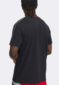 T-shirt nero in cotone a maniche corte, con nastro logo "Under Armour" lungo le cuciture delle spalle. Taglio semplice e rilassato con una texture morbida.