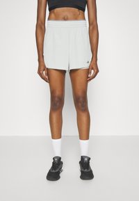 Pantaloni sportivi grigio chiaro con cintura elastica, tasche laterali e logo Adidas in basso a sinistra. Indossati con scarpe da ginnastica nere e calze bianche.