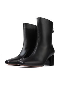 Bottines en cuir noir avec un bout pointu, une texture lisse et un talon épais. Détails de coutures et une discrète languette à l'arrière.