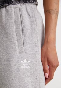 Pantalons de survêtement gris en tissu doux avec une coupe décontractée, dotés de poches latérales et d'un logo Adidas blanc sur la cuisse gauche.