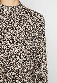 Vestido com padrão de leopardo e gola alta, feito de tecido suave; apresenta grandes manchas pretas sobre um fundo creme e uma cintura franzida.
