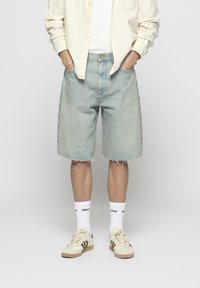 Light blue denim shorts with a loose fit, frayed hem, and visible stitching; paired with white socks and cream sneakers.