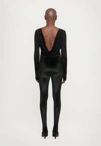 Black bodysuit with a draped deep back neckline and long sleeves, paired with high-waisted, shiny black leggings and stiletto heels.
