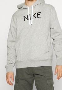 Gray hoodie made of cotton blend, featuring a front pocket, ribbed cuffs, and a drawstring hood. Black "NIKE" logo prominently displayed.