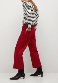 Pantalones de algodón rojos de pierna ancha con dobladillos deshilachados, combinados con una blusa de rayas en blanco y negro de manga larga y botas de tobillo negras con punta.
