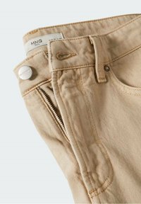 Pantalon beige en coton avec fermeture éclair à l'avant, bouton métallique marqué "MNG DENIM", passants de ceinture et étiquette de taille intérieure blanche.