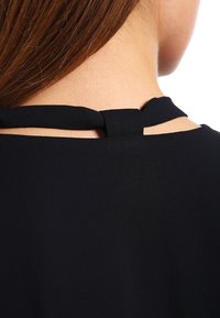 Musta mekko, jossa on halkio yksityiskohtana takaniskassa, valmistettu sileästä kankaasta yksinkertaisella muotoilulla ja saumattomalla viimeistelyllä.