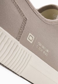 Beige plátěné tenisky s bílou gumovou podrážkou. Obsahují pro texturovanou stranu, detaily šití a vytištěný motivační text na svršku.