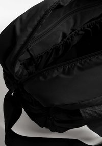 Črna tkanina torba za preko rame z več žepki z zadrgo in teksturirano površino, opremljena z oblazinjenim naramnim trakom in elastičnim robom.