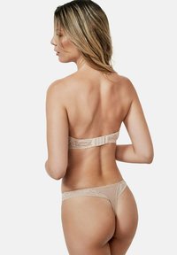 String en dentelle chair avec un délicat motif floral et une texture douce, présentant une large bande en dentelle et une fermeture ajustable à crochets.