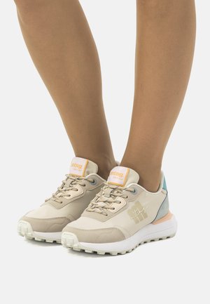 Zapatillas deportivas beige con parte superior sintética texturizada, acentos en azul y durazno, diseño con cordones y suela blanca gruesa con tracción.
