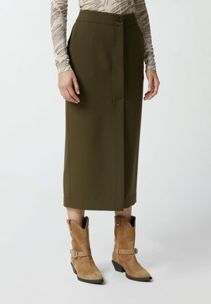 Jupe midi vert olive avec un pli avant et une fermeture à un seul bouton, assortie à des bottes de cowboy en daim tan avec une sangle et un bout pointu.
