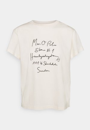 Cream cotton t-shirt with a relaxed fit. Features black handwritten text including a brand name and address. Short sleeves and crew neckline.