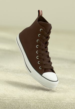Brązowy sneaker z wysoką cholewką, białą gumową podeszwą i noskiem, czarnym paskiem oraz materiałową pętelką z czerwono-białymi paskami.