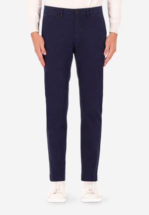 Pantaloni chino blu navy a taglio slim, realizzati in tessuto misto cotone. Presentano chiusura con bottoni, tasche angolate e orlo semplice. Abbinati a sneakers bianche.
