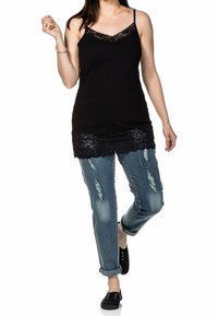 Top negro de tirantes con borde de encaje en el dobladillo, acompañado de jeans azul claros desgastados. Estilo casual que complementa unos zapatos negros sin cordones.